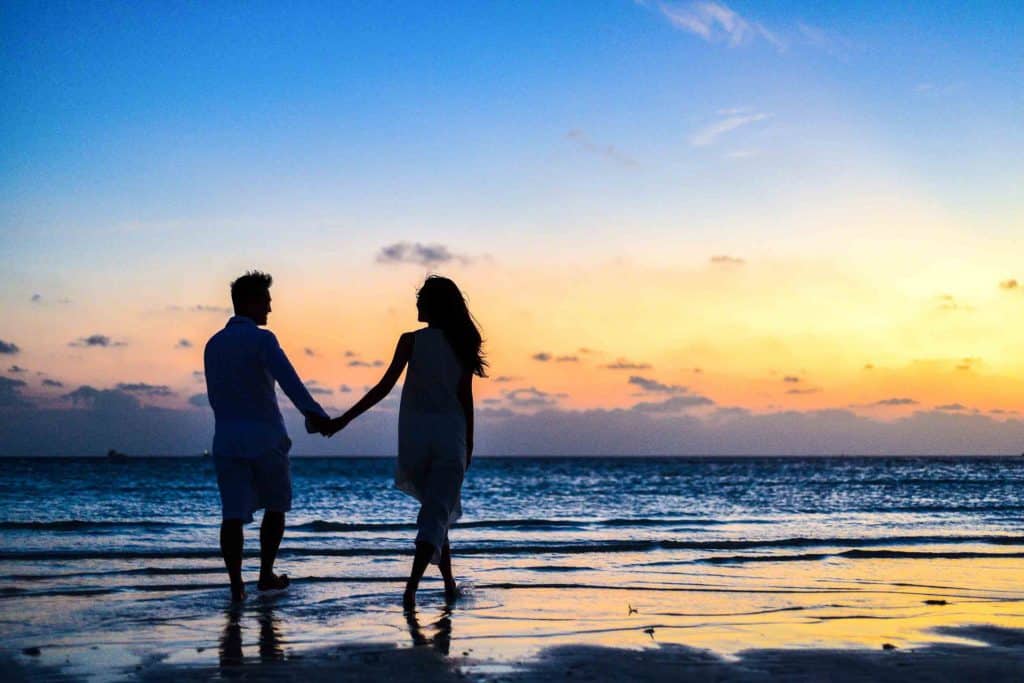 זוג כלה וחתן הולכים לאורך החוף בשקיעה